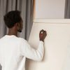 Back view of a man writing on a whiteboard during a presentation indoors.