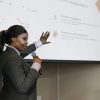 Businesswoman presenting with microphone, discussing improvements with a slide projection in a conference room.